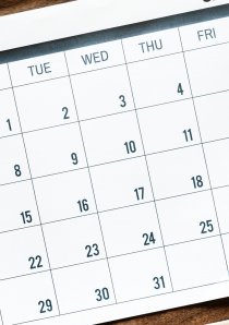 a desk calendar next to an alarm clock on a wooden desk surface