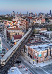 L train passing through the Bucktown neighborhood in Chicago with the city skyline and a color mural in the background