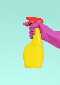 a person wearing pink rubber glove holds a yellow bottle of disinfectant spray