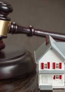 a wooden judge's gavel resting on desk beside model of a house