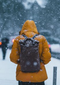 a person wearing a yellow park and black backpack standing on a snow covered sidewalk in Chicago