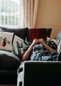 person lying on couch in apartment while reading a book
