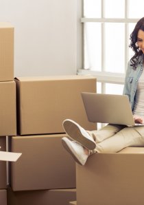 a young woman using a laptop while sitting atop apartment moving boxes